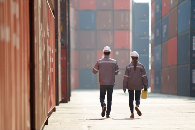 Two workers walking between shopping containers.