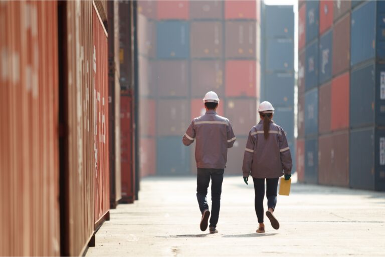 Two workers walking between shopping containers.