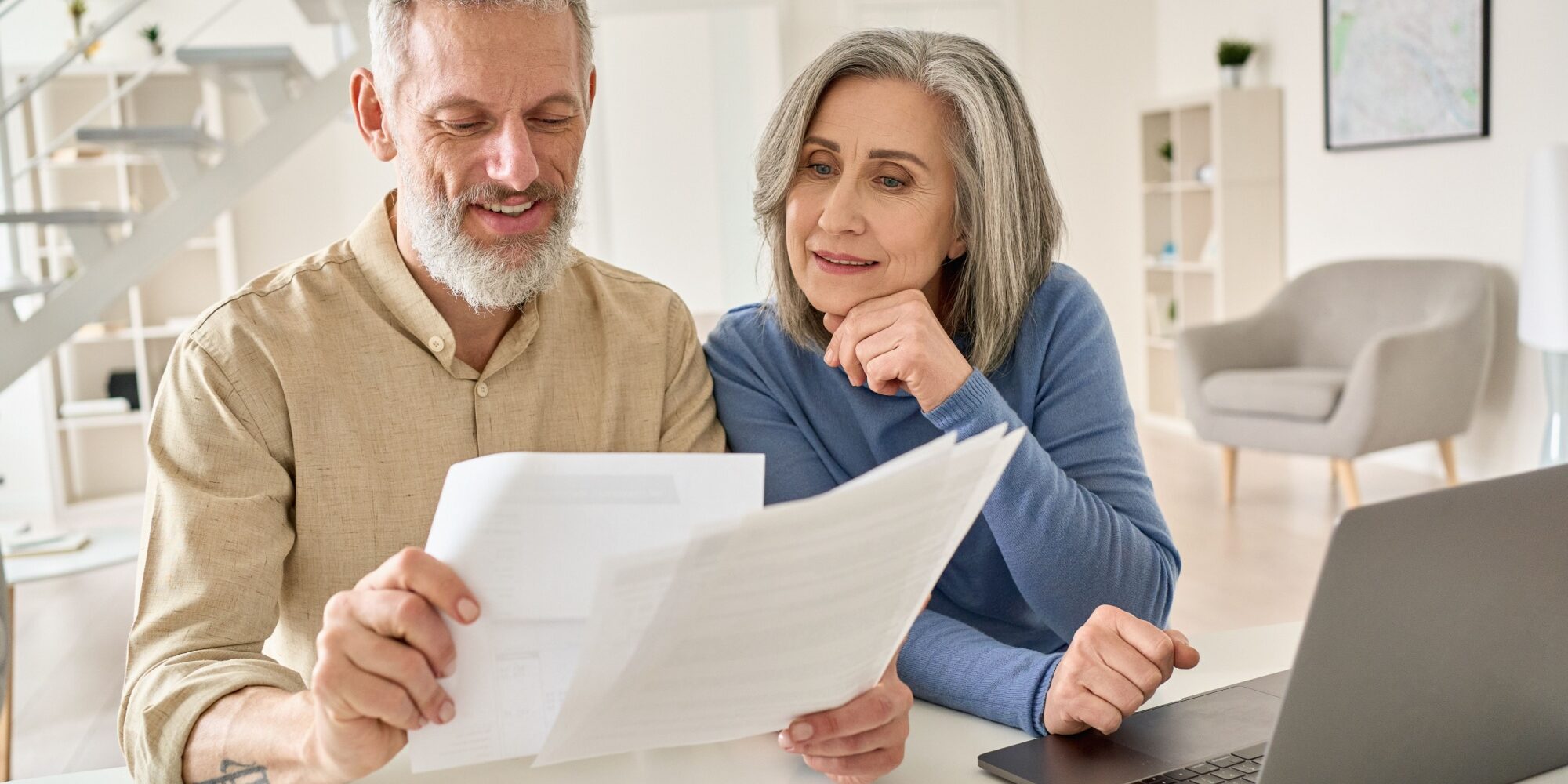 A senior couple sit at a laptop comparing multiple documents
