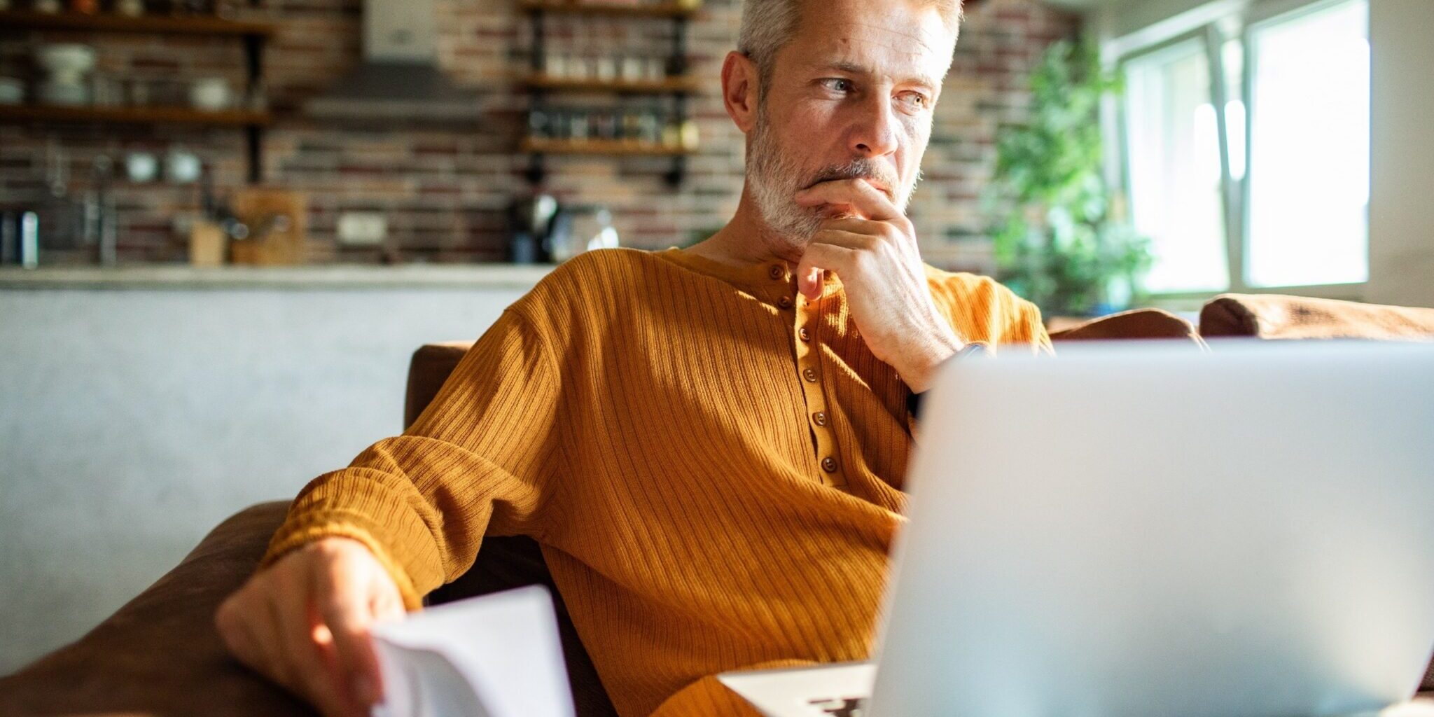 A man in his 50s thinking while using a laptop