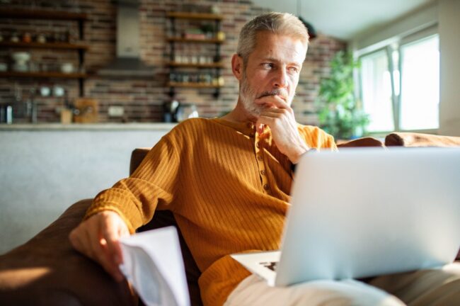 07 A man in his 50s thinking while using a laptop